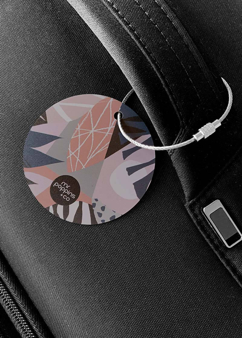 Metal luggage tag in pink dusk print on a black suitcase