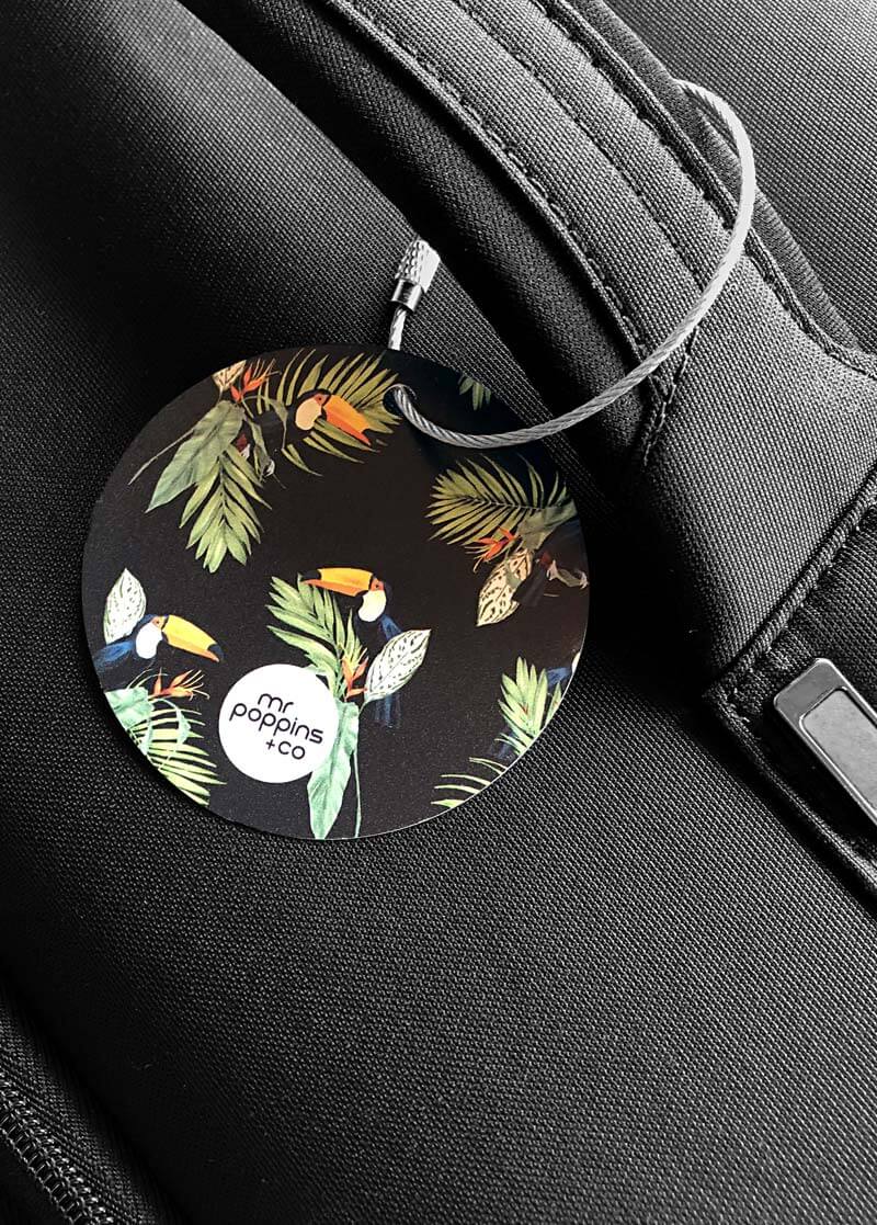 Metal luggage tag in toucan print on a black suitcase